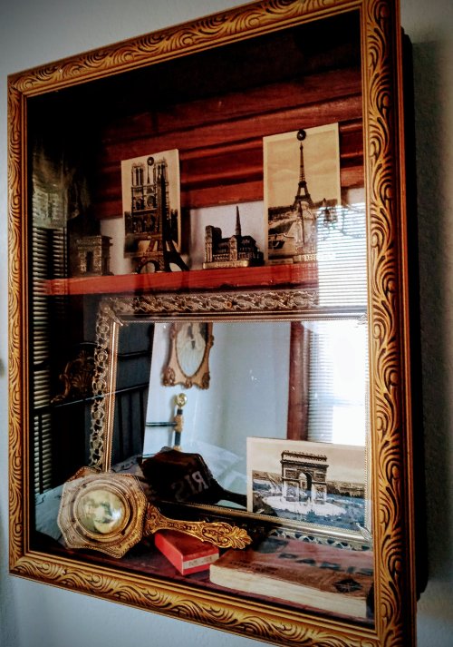 A vintage display case featuring framed photos of famous landmarks and decorative items, including a mirror and ornate frame.