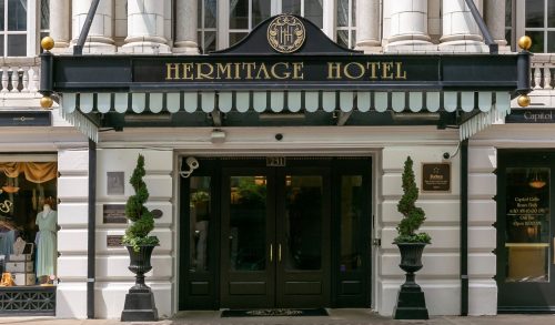 Facade of the Hermitage Hotel featuring elegant columns and a black awning with the hotel name displayed prominently.