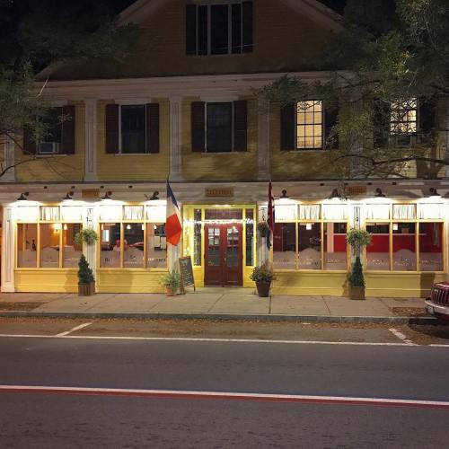 A charming restaurant with yellow exterior, French flags, and warm lighting, set on a quiet street at night.