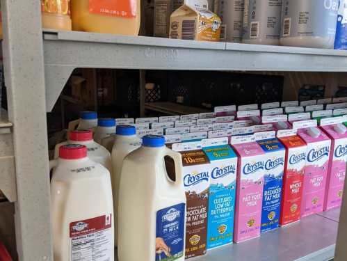 Shelves stocked with various milk cartons and bottles, including whole, low-fat, and chocolate milk options.