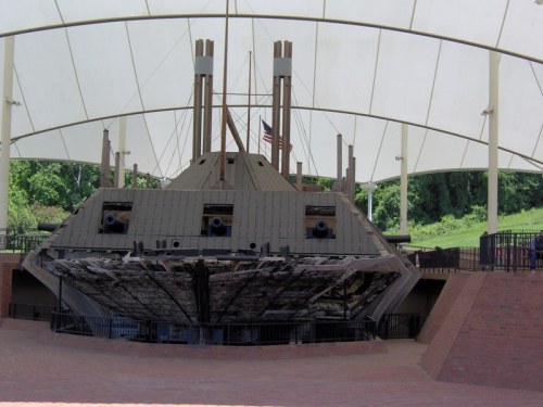 Historic ship displayed under a large canopy, showcasing its wooden structure and cannons, with an American flag in the background.