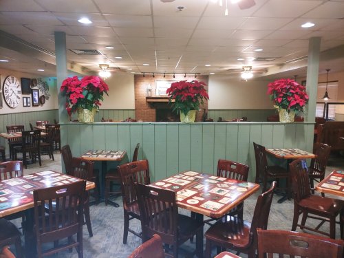 Cozy restaurant interior with wooden tables, chairs, and festive poinsettias on display near a brick fireplace.