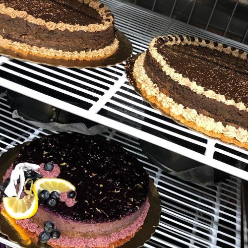 Two chocolate cakes displayed on a shelf, one with a dark chocolate layer and the other topped with berries and lemon.
