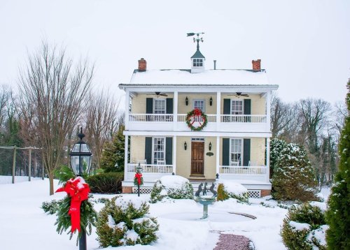 A charming two-story house decorated for winter, with snow-covered roofs, a wreath, and festive red bows.