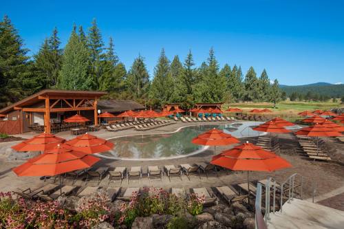 A scenic pool area surrounded by orange umbrellas, lounge chairs, and lush greenery under a clear blue sky.