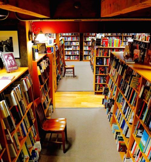 A cozy library with wooden shelves filled with books, a chair in the foreground, and a warm light illuminating the space.