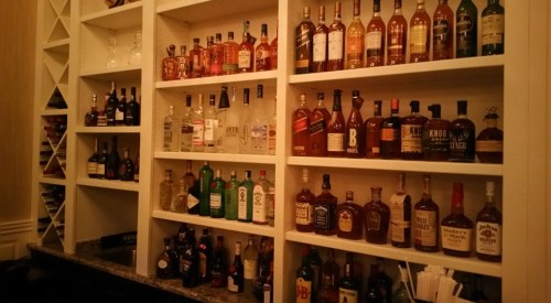 A well-stocked bar with various bottles of liquor displayed on white shelves against a light background.