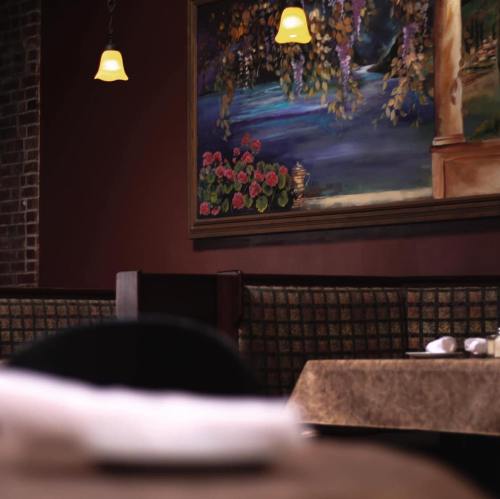 A cozy restaurant interior featuring a floral painting, warm lighting, and neatly set tables.