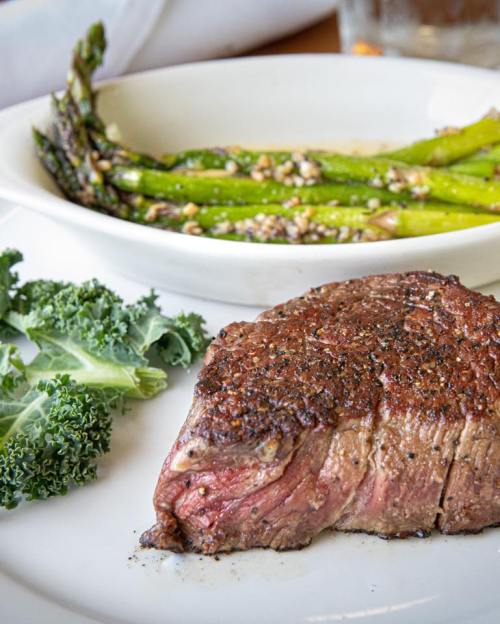A perfectly cooked steak with a side of asparagus and kale on a white plate.