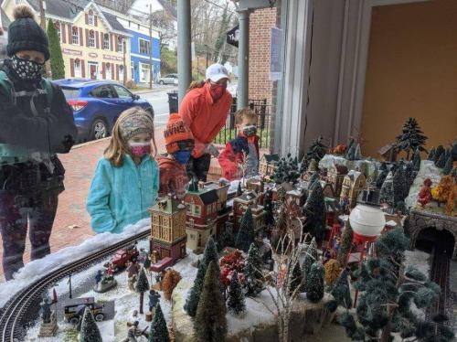 A family admires a detailed miniature winter village display through a shop window.