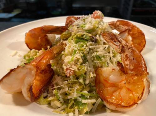 A plate of shrimp atop a bed of shredded greens, garnished with cheese and herbs.