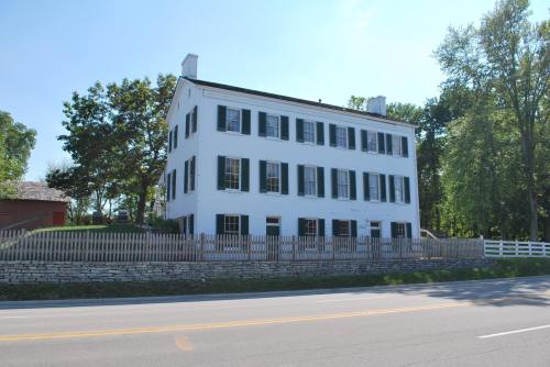 A white, two-story house with green shutters, surrounded by a wooden fence and trees, viewed from the street.