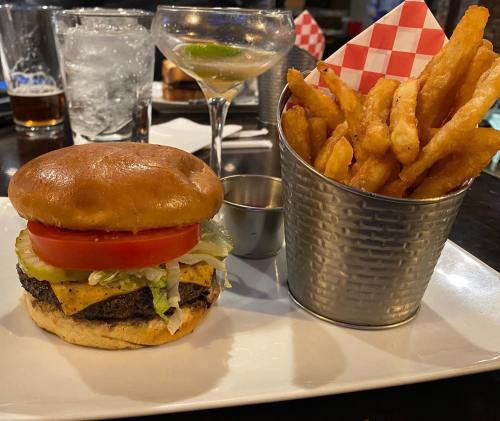 A juicy burger with lettuce, tomato, and cheese, served with a side of sweet potato fries and a cocktail.