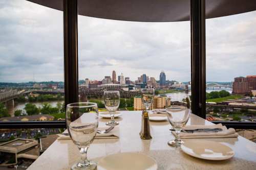 A dining table set with glasses overlooks a city skyline through large windows.