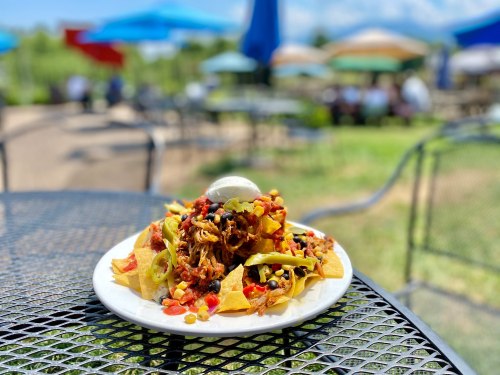 A plate of nachos topped with pulled pork, corn, jalapeños, and a dollop of sour cream, set on a sunny outdoor table.