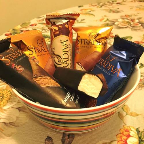 A colorful bowl filled with assorted Stradiva chocolate bars on a floral tablecloth.