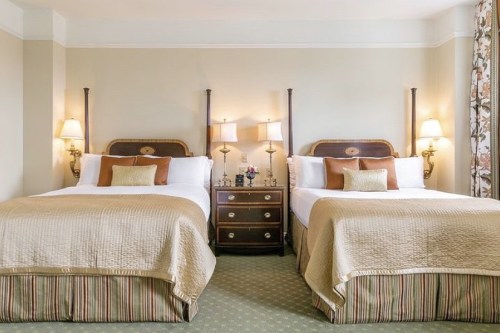 A cozy hotel room featuring two beds with decorative headboards, bedside lamps, and a small dresser.