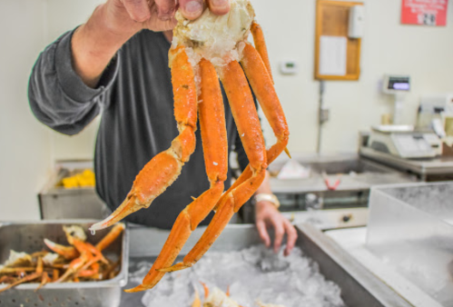 A person holds a large, cooked crab leg above a tray of ice in a seafood market.
