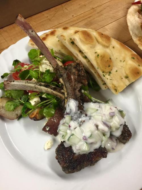 A plate featuring grilled lamb chops with cucumber sauce, a fresh salad, and pieces of flatbread.