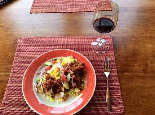 A plate of colorful rice topped with meat and vegetables, accompanied by a glass of red wine on a wooden table.