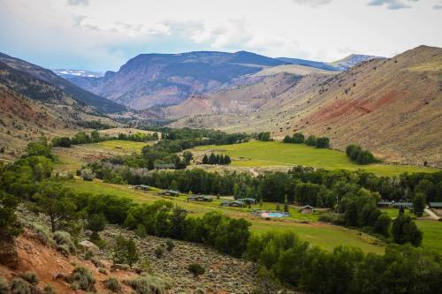 A scenic view of rolling hills and mountains, with a lush green valley and small buildings nestled among trees.