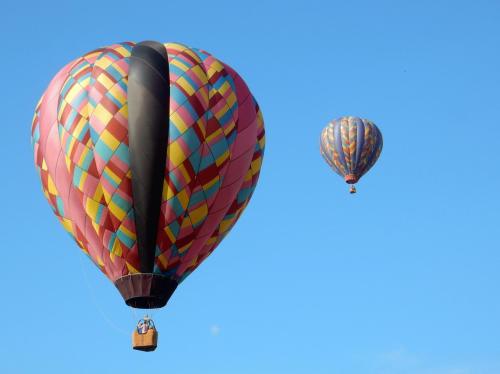 Two colorful hot air balloons float against a clear blue sky.