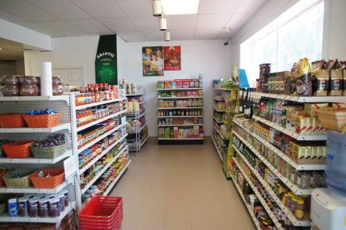 A well-stocked grocery aisle with shelves of various food products, snacks, and beverages. Brightly lit and organized.