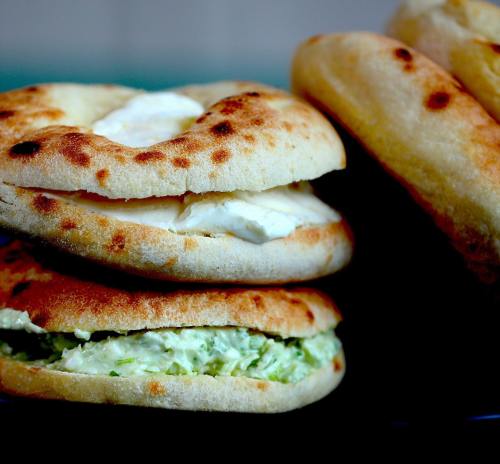 Three toasted flatbreads filled with creamy white cheese, stacked on a dark plate.