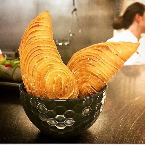 A bowl filled with two golden, spiral-shaped pastries on a wooden surface.