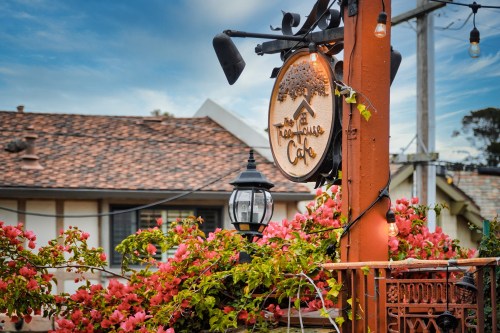 A charming café sign surrounded by vibrant pink flowers and a rustic building in the background.