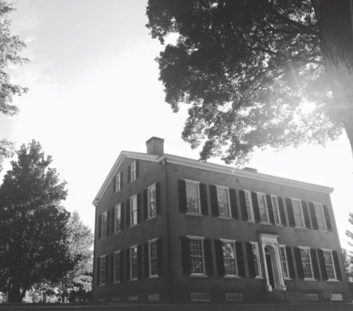 Historic building with large windows and a central door, surrounded by trees, captured in black and white.