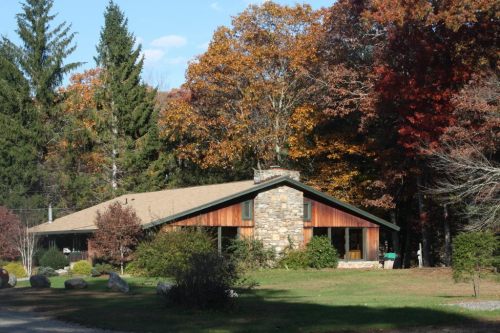 A cozy stone and wood house surrounded by colorful autumn trees and greenery.