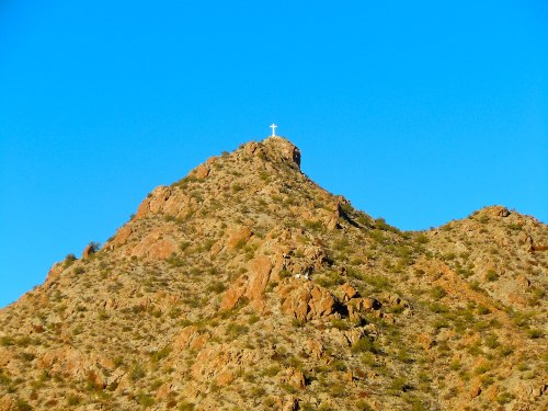 A rocky mountain peak under a clear blue sky, topped with a white cross.
