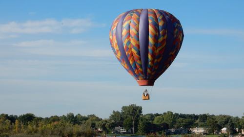 A colorful hot air balloon floats above a scenic landscape under a clear blue sky.