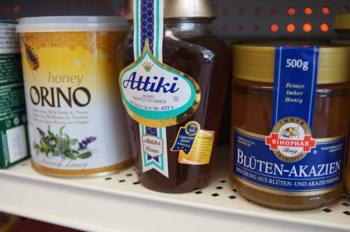 Three jars of honey on a shelf: Orino honey, Attiki honey from Greece, and Bhophar acacia honey.