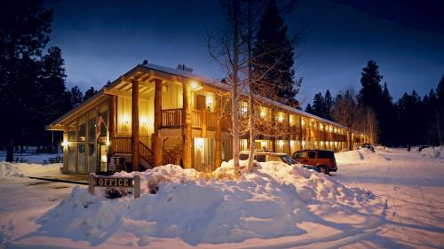 A cozy lodge at night, illuminated warmly, surrounded by snow-covered ground and tall trees.