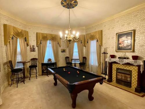 A stylish room with a pool table, elegant curtains, a chandelier, and a fireplace, creating a cozy atmosphere.