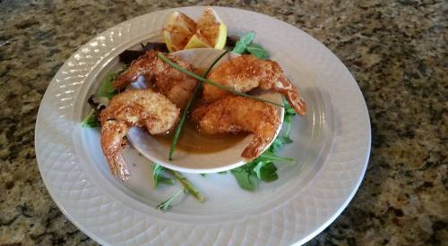 A plate of crispy fried shrimp served with a dipping sauce and garnished with lemon wedges and greens.