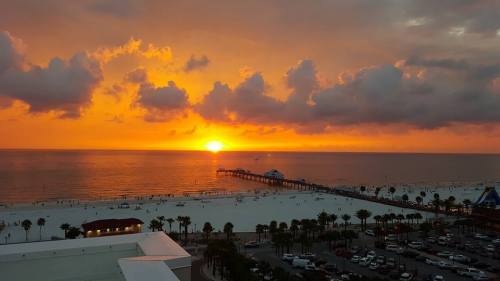A vibrant sunset over the ocean, with clouds and a pier extending into the water, surrounded by a sandy beach.