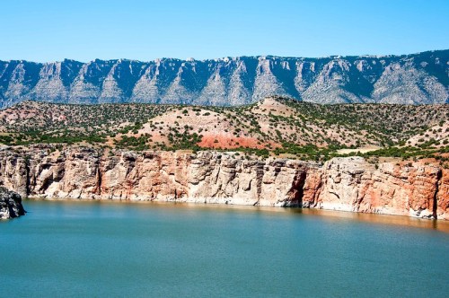 A serene lake surrounded by rocky cliffs and mountains under a clear blue sky.