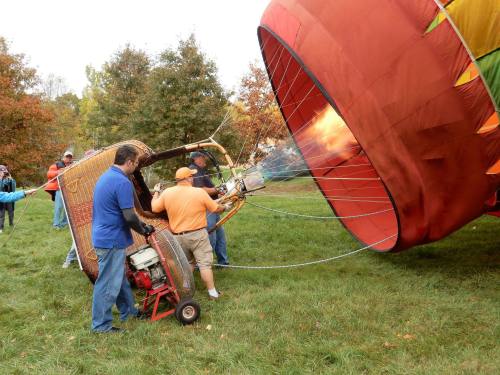 A hot air balloon being inflated, with crew members operating the burner and preparing for flight on a grassy field.