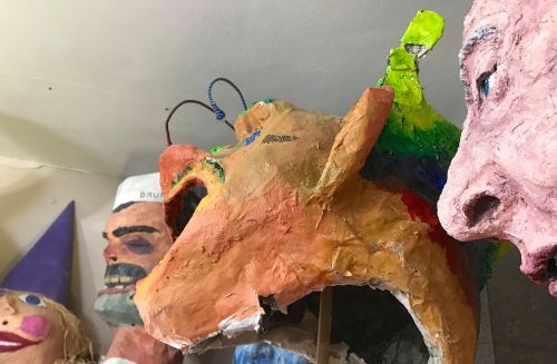 Colorful, abstract masks and sculptures displayed on a shelf, featuring various exaggerated facial features.