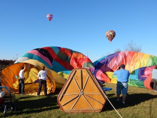 Colorful hot air balloons being inflated on a sunny day, with people preparing for a flight in the background.
