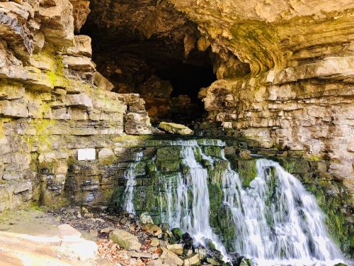 A serene cave entrance with a small waterfall cascading over moss-covered rocks.