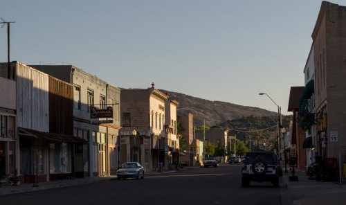 Quiet street in a small town, featuring historic buildings and a mountain backdrop under a clear sky.