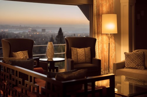 Cozy lounge area with two armchairs, a lamp, and a view of a city skyline at sunset.