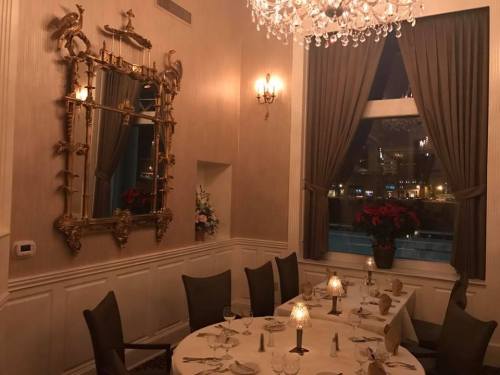 Elegant dining room with a chandelier, ornate mirror, and a table set for a formal dinner, featuring window views at night.