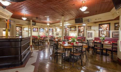 Cozy restaurant interior with wooden tables, chairs, and decorative walls, featuring a bar and floral centerpieces.