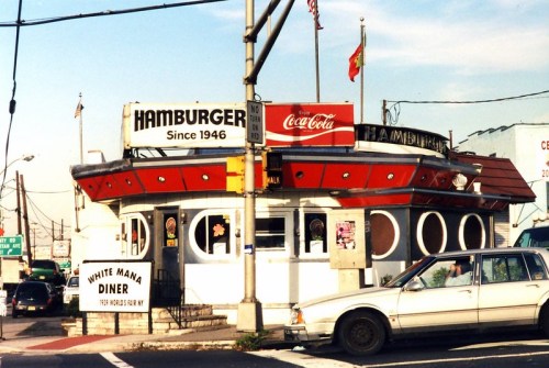 A vintage diner with a round design, featuring a red roof and signs for hamburgers and Coca-Cola.