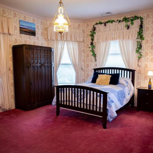Cozy bedroom with a wooden bed, decorative curtains, a nightstand, and a vintage wardrobe on a red carpet.